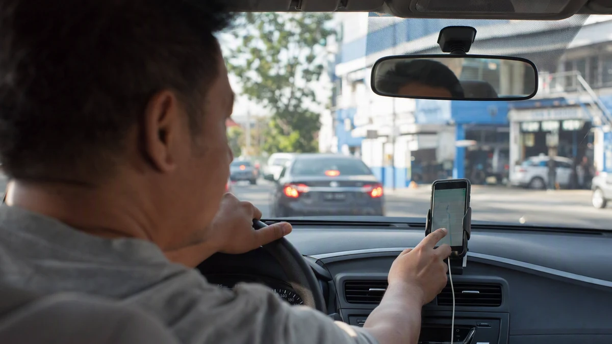 Motorista consultando aplicativo de navegação no celular dentro do carro, próximo a uma oficina